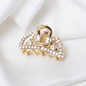 Détail d'une petite pince à cheveux dorée avec strass sur un fond de tissu en soie blanche