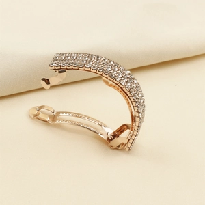 Détail d'une pince à cheveux en or rose sertie de strass brillants sur tissu beige