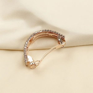 Détail d'une pince à cheveux en or rose avec des strass brillants sur tissu beige