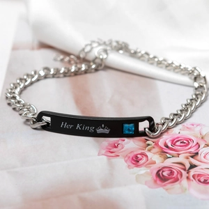 Close-up of silver Cuban link bracelet with black 'Her King' plate and blue zircon