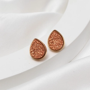Detailed macro view of orange pink teardrop druzy earrings with gold textured edges