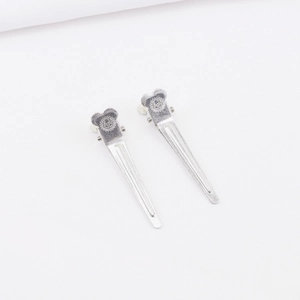 Detailansicht silberner Entenschnabel-Haarklammern mit geprägtem Zahnrad-Logo auf Metall
