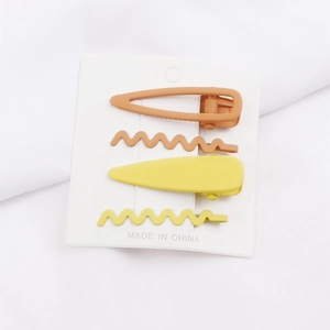 Détail de pinces à cheveux géométriques mates en métal jaune et orange sur leur carte