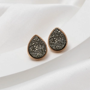 Close-up of minimalist teardrop earrings with gold trim and dark grey crystal drusy