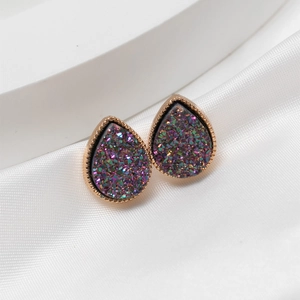 Detail of rose gold teardrop studs with purple and green resin crystals on white satin