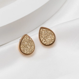 Detailed close-up of golden teardrop earrings with sparkling crystal texture and beaded edges