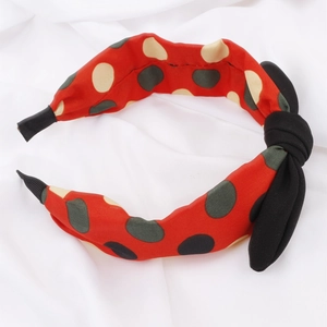 Vue détaillée d'un serre-tête rouge à pois avec un nœud noir sur tissu blanc