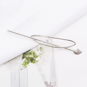 Detail view of silver hollow oval hair stick with textured leaf charm on white fabric
