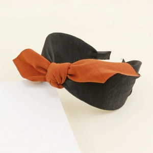 Détail d'un serre-tête noir large avec un nœud papillon en tissu orange brûlé