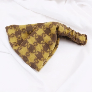 Close-up of yellow and brown checkered knitted headband on white fabric texture