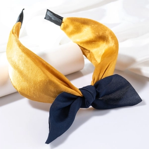 Détail du serre-tête en soie jaune avec nœud bleu marine et texture de tissu torsadé