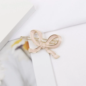 Détail d'une barrette noeud en émail rose avec finition en métal doré et texture lisse