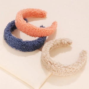 Close-up of three plush lamb wool headbands in orange, navy blue, and beige colors