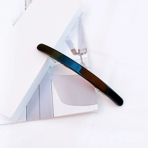 Detail of a minimalist black acetate hair clip with a glossy mirror finish on a magazine
