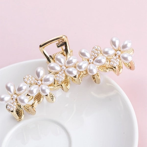 Elegant gold metal hair claw clip with large pearl flowers and spring on a pink background