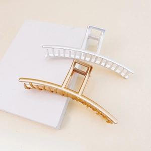 Detail view of minimalist matte gold and silver metal claw clips on white platforms