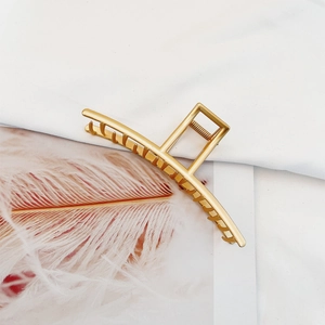 Close-up of golden matte metal shark hair claw clip on elegant white fabric background