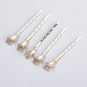 Detail view of five gold-plated skeleton hand bobby pins arranged on a grey background
