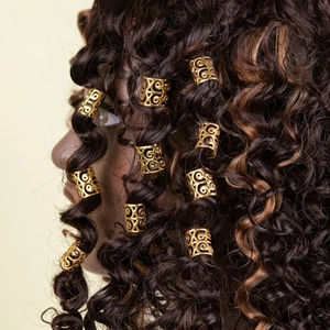 Golden hollow hair rings with intricate patterns on dark brown braided hair