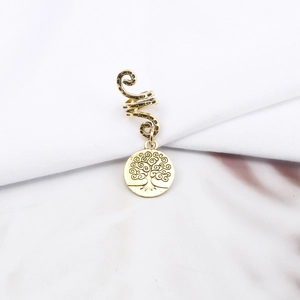 Detail of golden spiral dreadlock hair accessory with life tree charm on white fabric