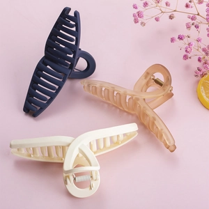 Three large matte hair claws in navy, amber and cream, set against a pink background
