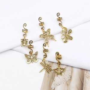 Detail of golden spiral dreadlock cuffs with butterfly and dragonfly charms on white background