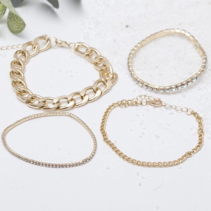 Vierteiliges Gold-Armband-Set mit Strasssteinen und Panzerkette auf weißem Sandhintergrund