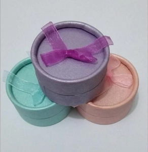 Three circular cardboard jewelry gift boxes with organza ribbon bows in purple green pink