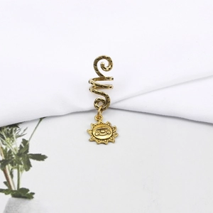 Detail of golden spiral dreadlock cuff with bohemian sun and eye charm on white fabric