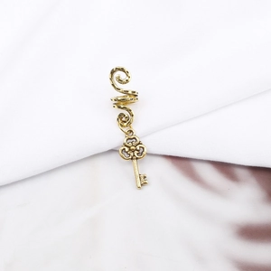 Detail of a golden alloy dreadlock cuff with a vintage spiral and key pendant