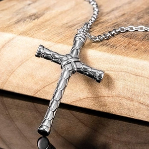 Macro detail of men's cross pendant featuring textured industrial scale design and O-chain