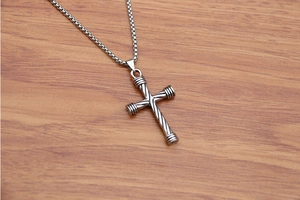 Macro detail of silver cross pendant with cable texture and classic box chain design