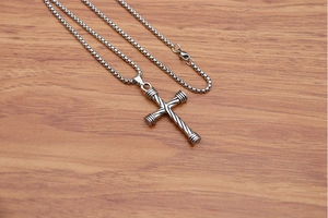 Macro shot of silver hip-hop cross pendant with twisted metal texture and box chain link
