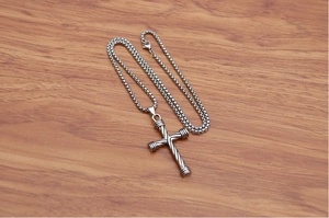 Detail of silver cross pendant with twisted rope texture and round box chain on wood