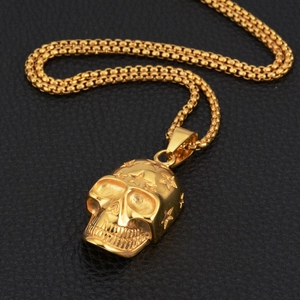 Macro detail of gold skull pendant with star engravings on a box chain necklace