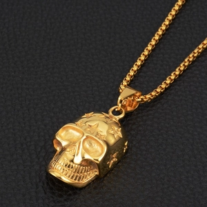 Macro shot of gold skull pendant with star relief and bead chain on leather