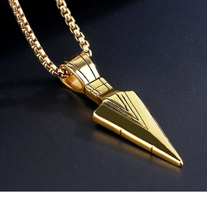 Macro shot of gold arrowhead pendant with box chain on dark textured background