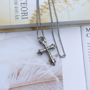 Détail du pendentif croix vintage avec gravure noire sur une chaîne à mailles carrées