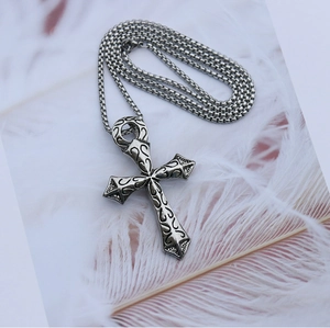 Détail du pendentif croix gothique argentée avec gaufrage floral sur plumes blanches