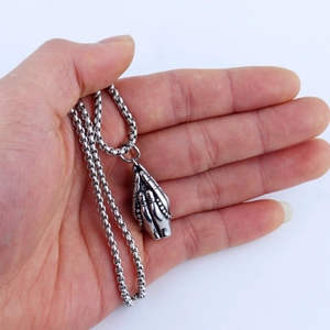 Macro shot of vintage stainless steel praying hands pendant on a polished ball chain