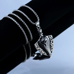 Gros plan du pendentif bouclier cobra argenté vintage avec chaîne sur support velours