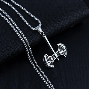 Close-up of double-bladed axe pendant with geometric carvings on a steel chain