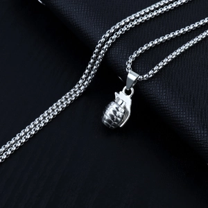 Detailed close-up of a silver grenade pendant on a square pearl chain against black leather
