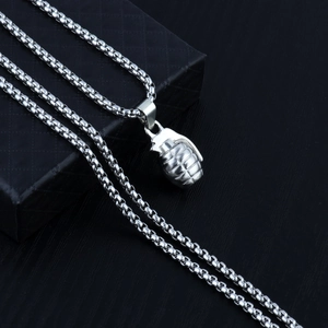 Close-up of a shiny silver grenade pendant on a box chain inside a black jewelry box