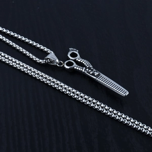 Vue détaillée du pendentif ciseaux et peigne en argent rétro sur fond de bois noir