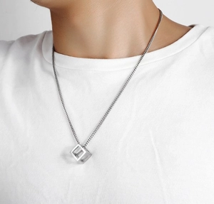 Detail of silver hollow cube pendant necklace on male model wearing white t-shirt