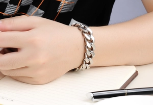 Close-up of a silver stainless steel Cuban link bracelet worn by a man in an office setting