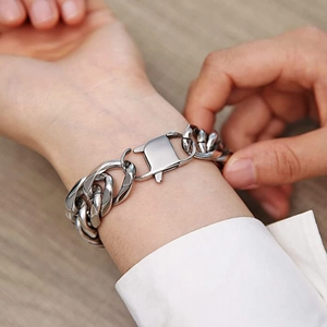 Close-up of a thick stainless steel Cuban link bracelet with a shield-shaped plug-in clasp