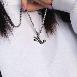 Detail of soccer shoe and ball pendant necklace in vintage silver finish on white hoodie