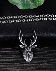 Detailed close-up of retro silver stag head pendant necklace on textured wood surface
